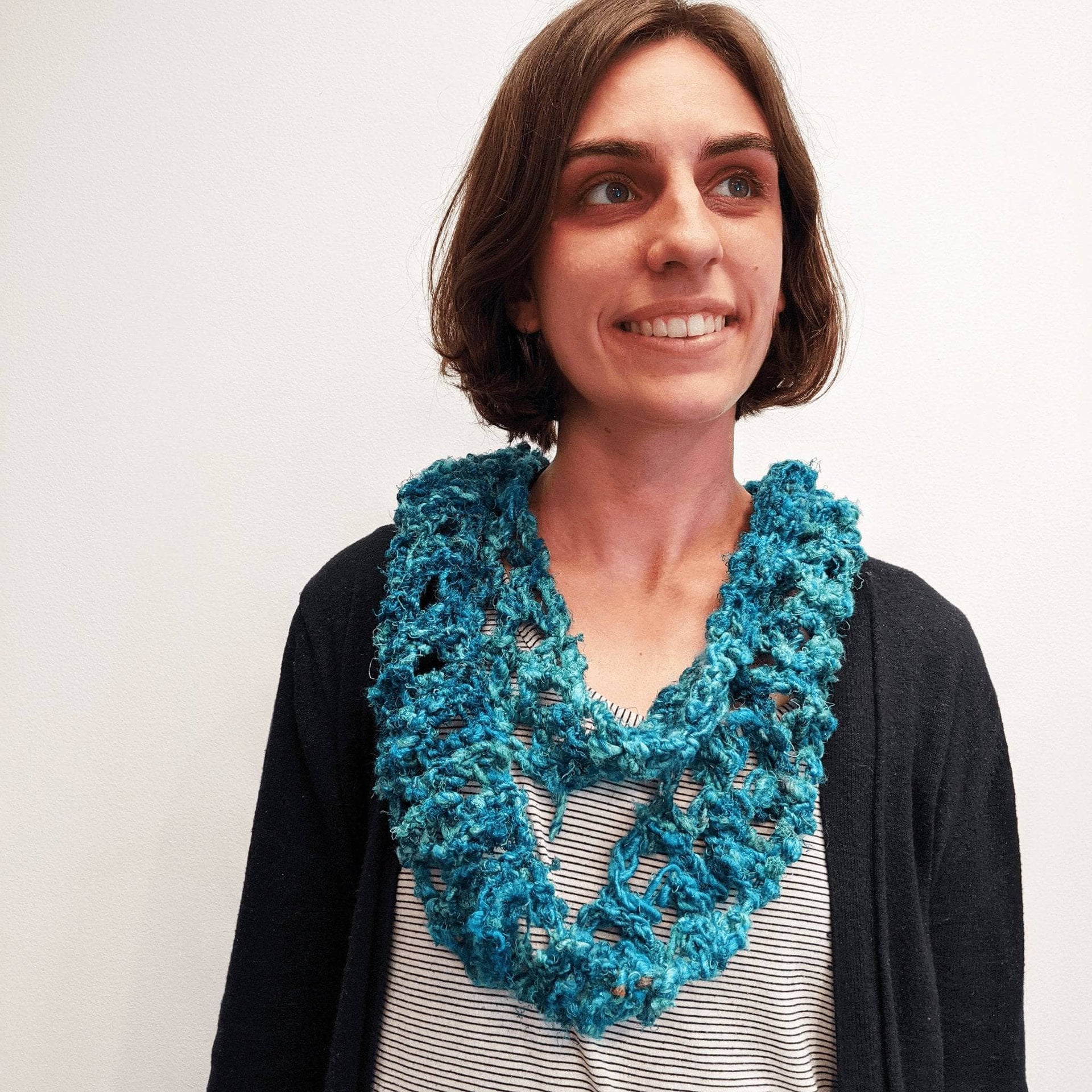 Finished infinity scarf in multi-tonal sea-glass and teal knit pattern draped over a shoulder