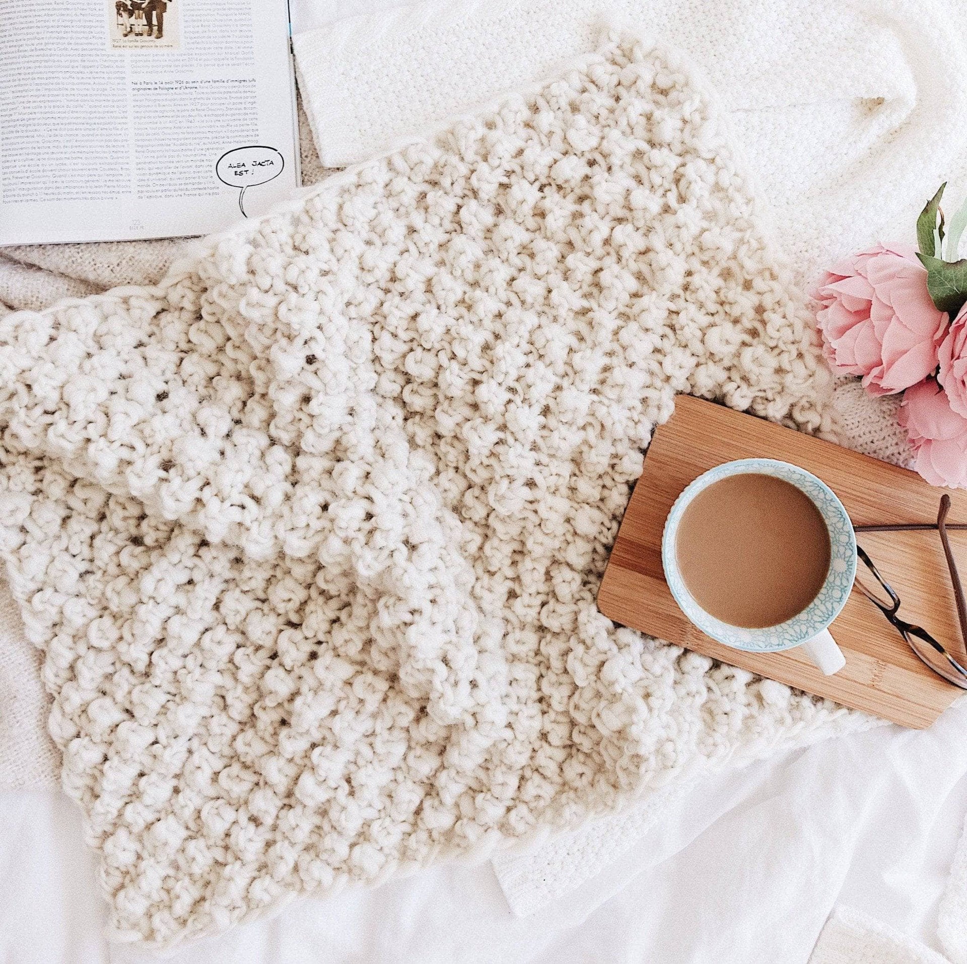 A soft, cream-colored Raspberry Dreams knit baby blanket styled in a modern, minimalist nursery setting.