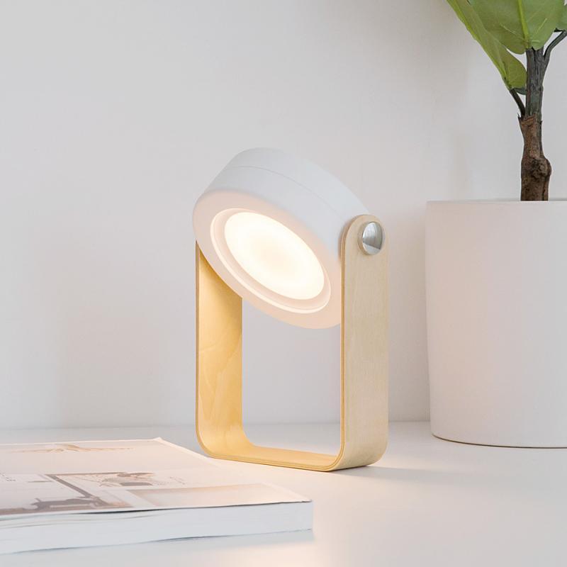 Retractable LED lantern lamp with wooden handle sitting on a bedside table.