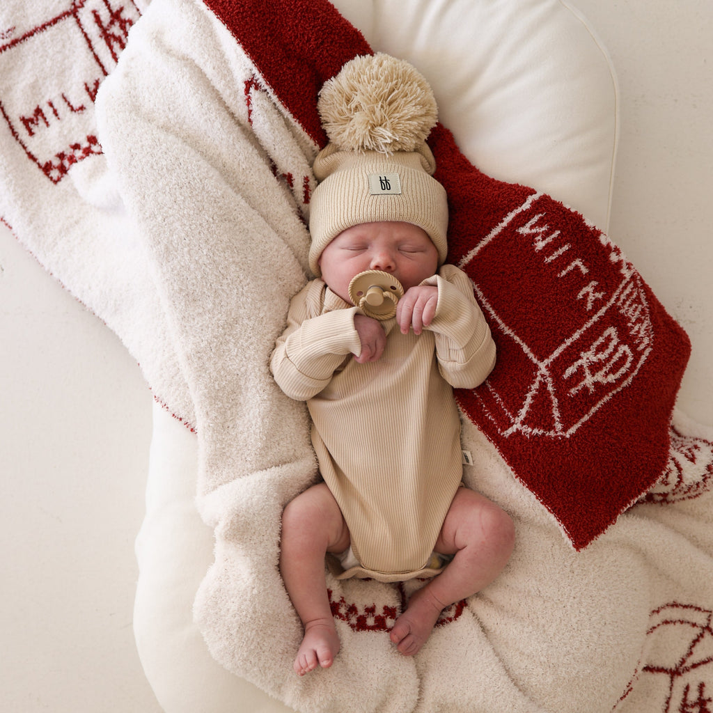 A newborn baby wearing a ribbed long sleeve bamboo snapsuit in cream color, lying on a soft textured blanket.