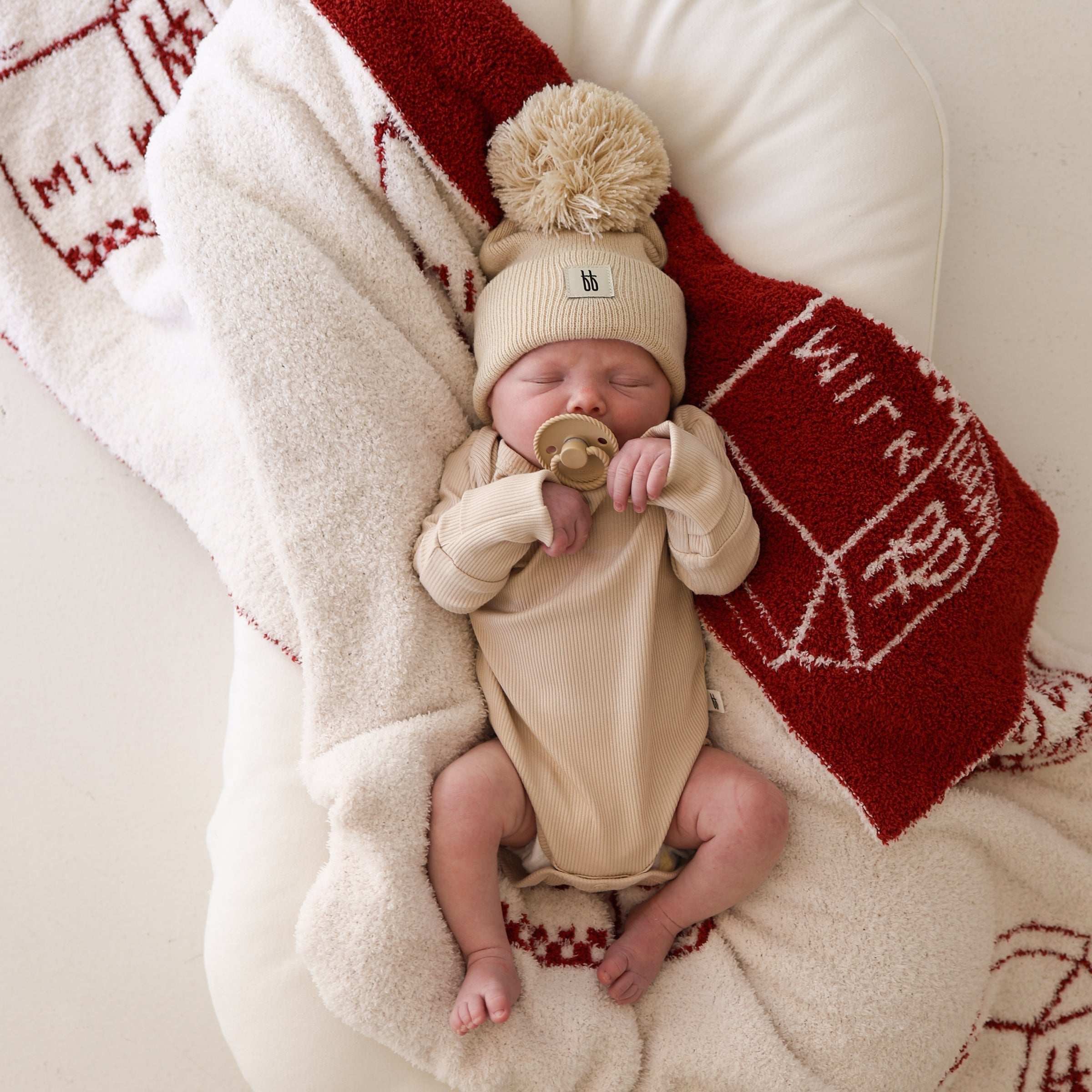 A newborn baby wearing a ribbed long sleeve bamboo snapsuit in cream color, lying on a soft textured blanket.