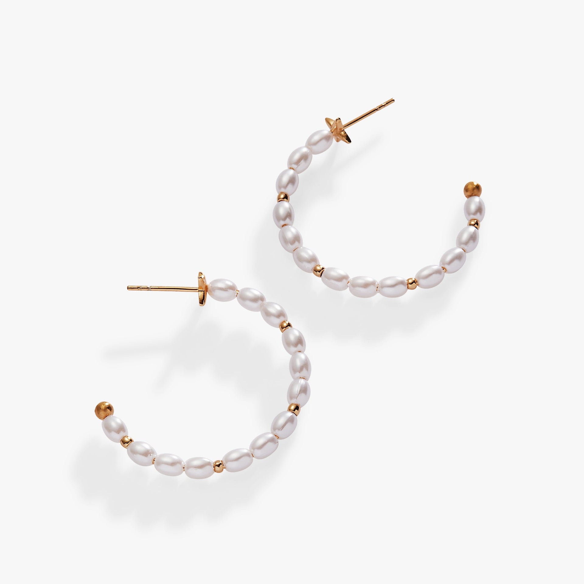 Gold hoop earrings decorated with white rice pearls, featuring a romantic minimalist aesthetic.