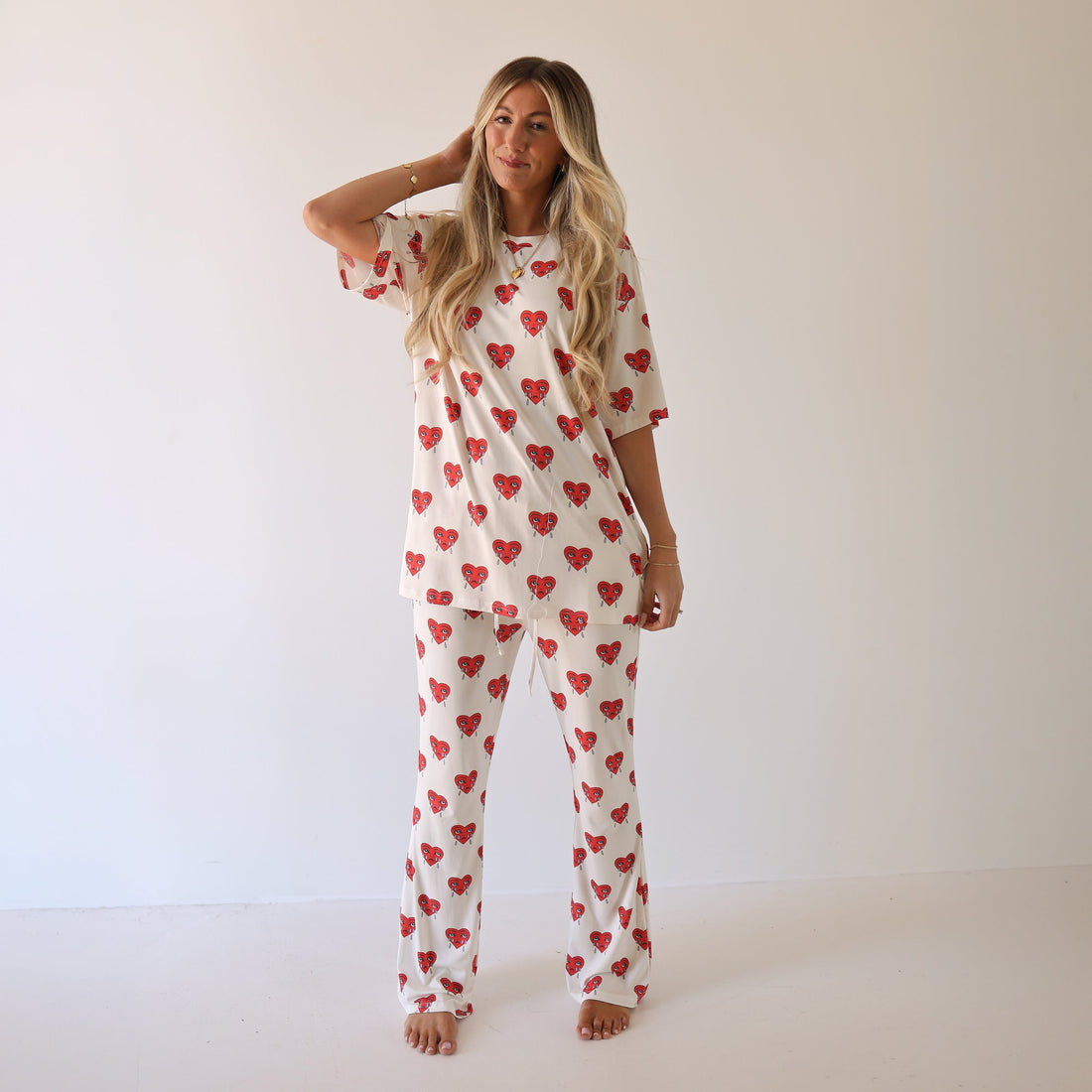 Woman wearing an oversized white short sleeve bamboo pajama top and matching flared pants with a red sad heart print.