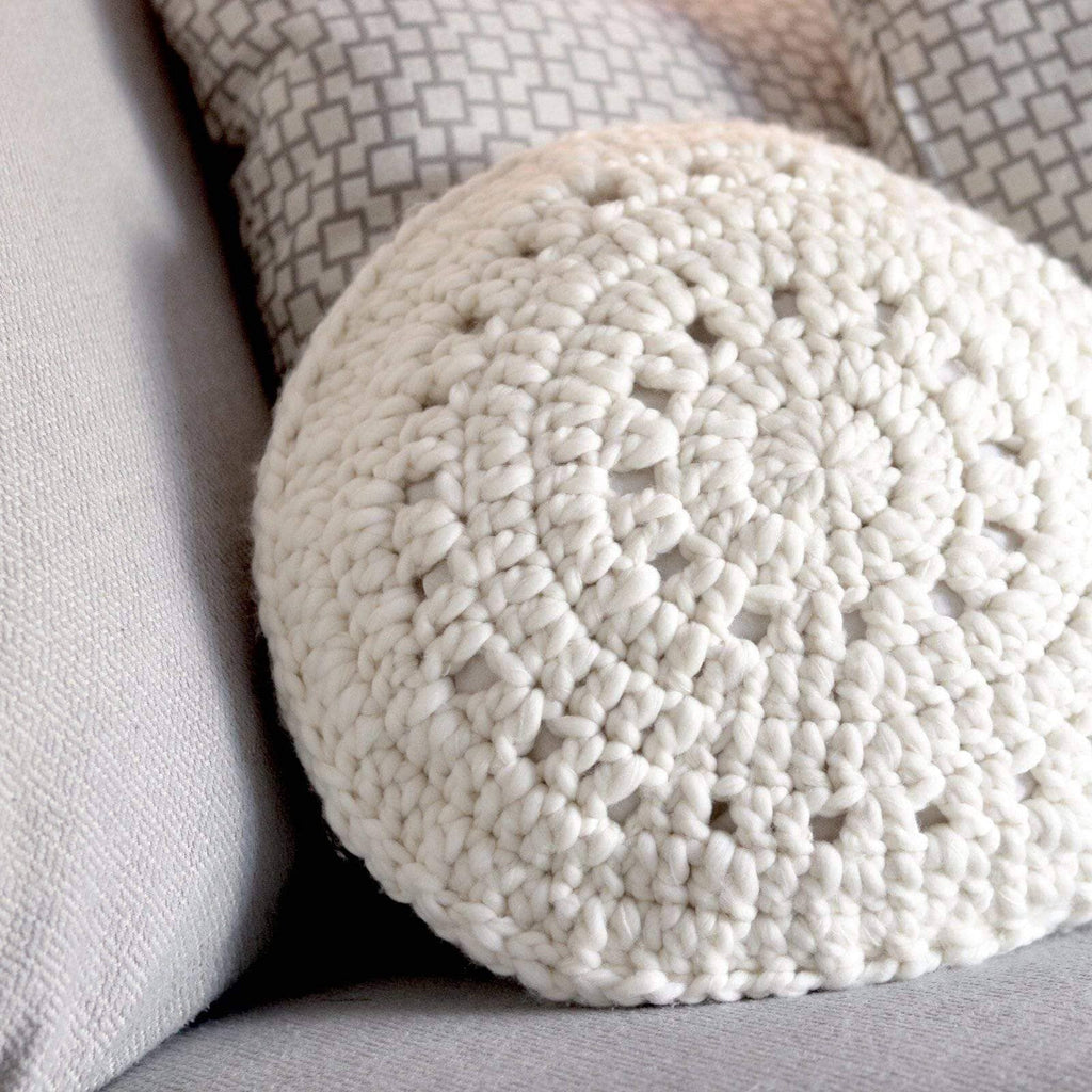 Round off-white knit throw pillow with sand dollar inspired geometric pattern on a neutral sofa