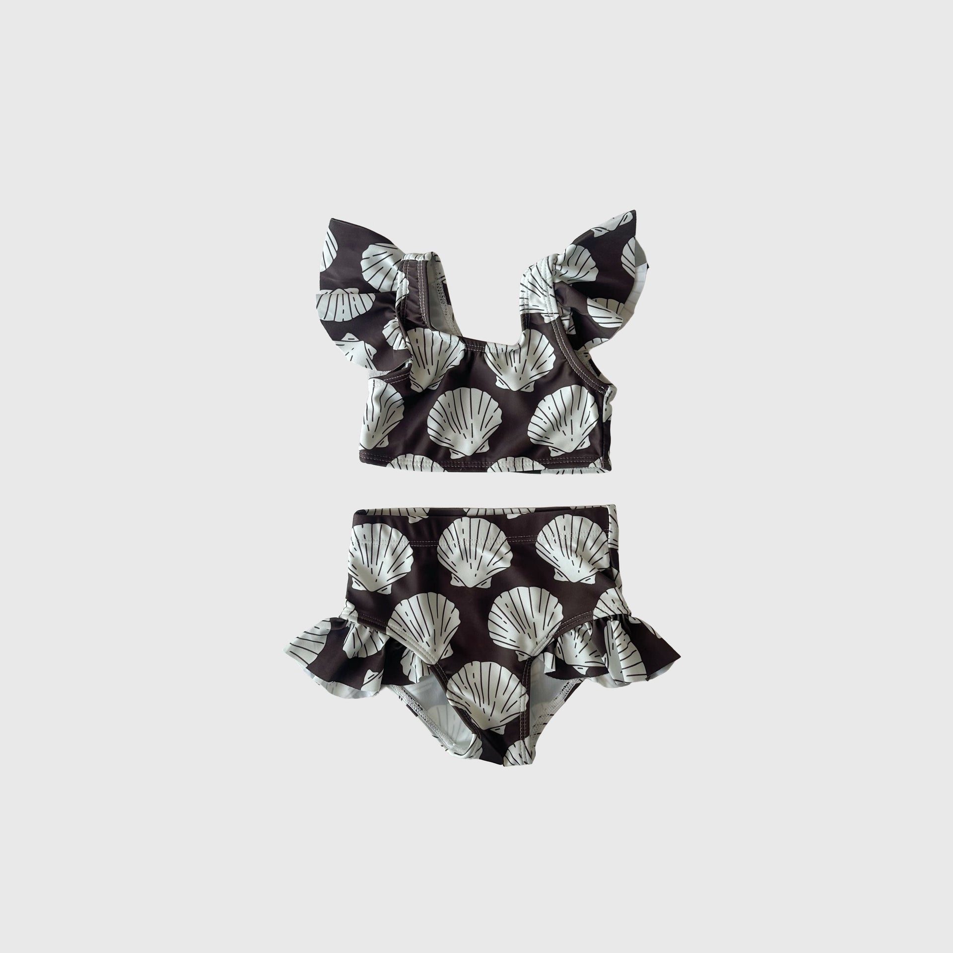 Girl wearing a dark brown and white two-piece swimsuit with a seashell print.