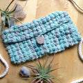 Shoreline Purse crochet kit featuring light blue and multi-colored speckled silk yarn on a textured surface