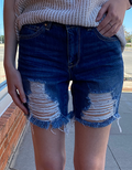 Model wearing high-rise medium blue denim mom shorts with frayed hem details in a casual streetwear setting.