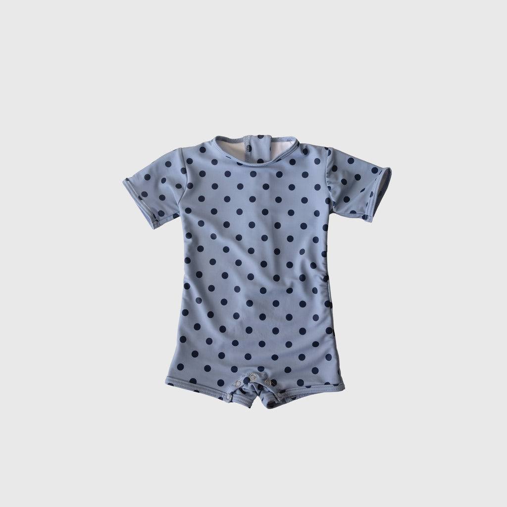 Baby wearing a navy and light blue polka dot shortie swimsuit with short sleeves and snaps.