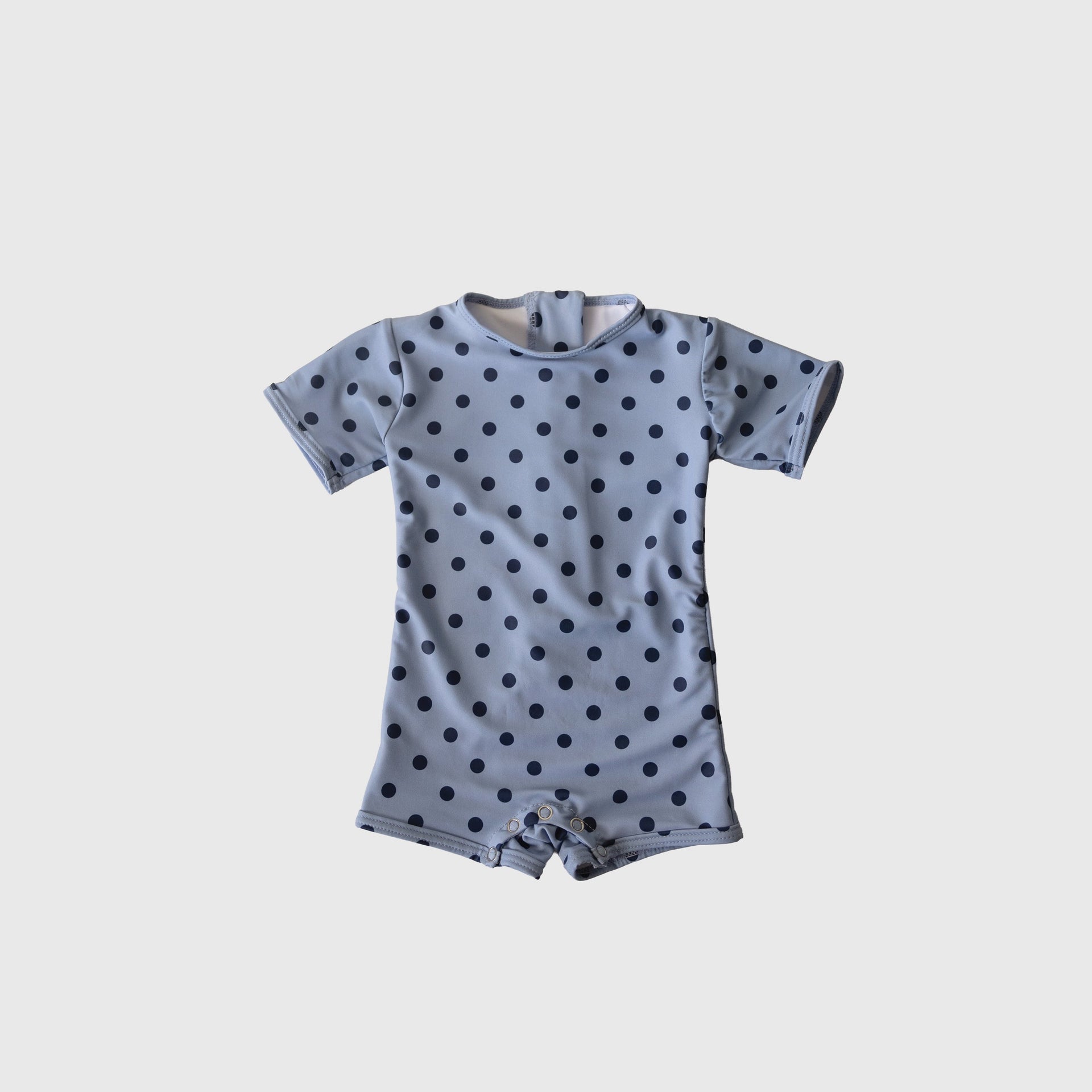 Baby wearing a navy and light blue polka dot shortie swimsuit with short sleeves and snaps.