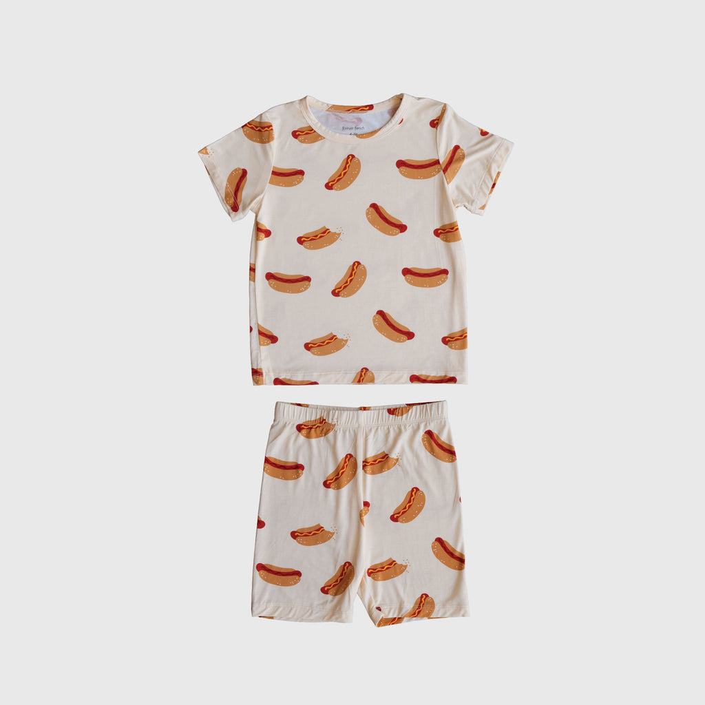 Child wearing a playful hot dog print bamboo short set with biker shorts in cream, brown, and red.