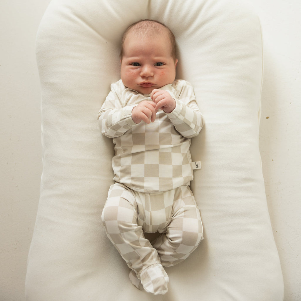 Infant wearing a beige and off-white geometric checkerboard footed lounge set.
