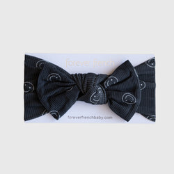 A charcoal grey ribbed baby head wrap with white smiley face line art and a decorative bow.
