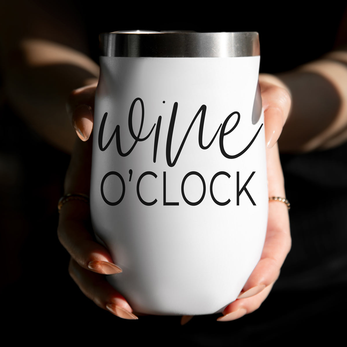 A person holding a white 17oz wine tumbler with the text Wine O'Clock in black font.