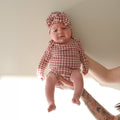 Baby wearing a long sleeve bamboo snapsuit in a red window pane pattern with a matching head wrap