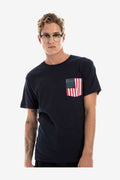 A man wearing a navy blue crew neck short-sleeve t-shirt with an American flag print pocket on the left chest.