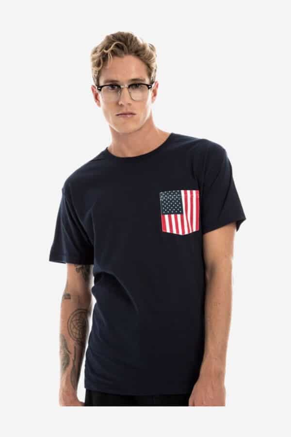 A man wearing a navy blue crew neck short-sleeve t-shirt with an American flag print pocket on the left chest.