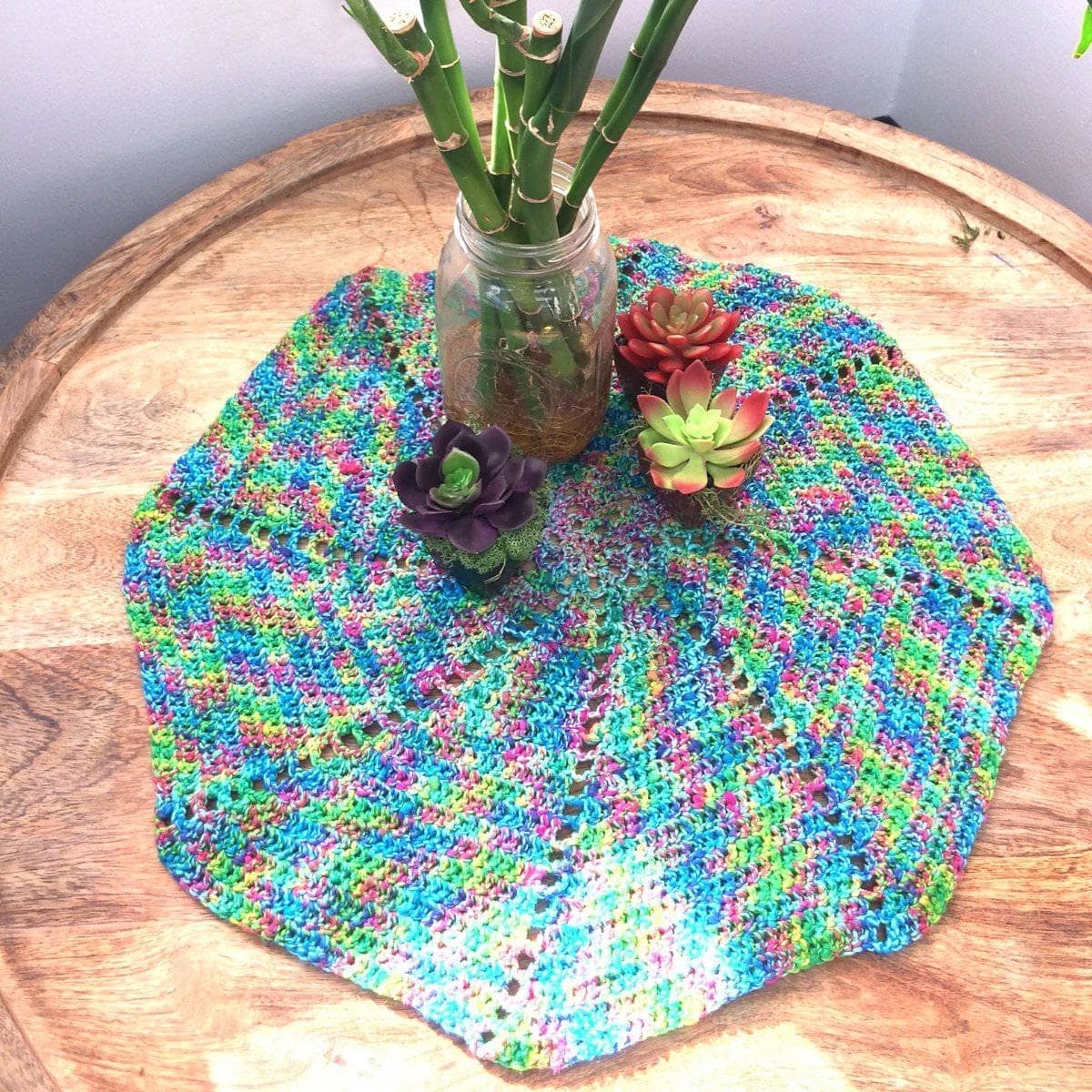 Vibrant multi-colored Spiral Fan Doily crochet kit displayed on a wooden surface in a bohemian styled room.