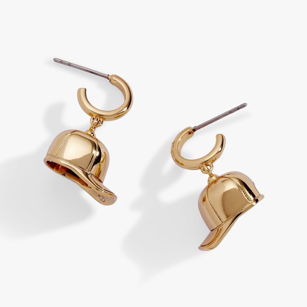 Modern gold huggie hoop earrings featuring dimensional baseball cap charms hanging from the base.