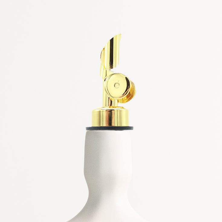 Gold colored self-closing metal bottle spout attachment on a white bottle