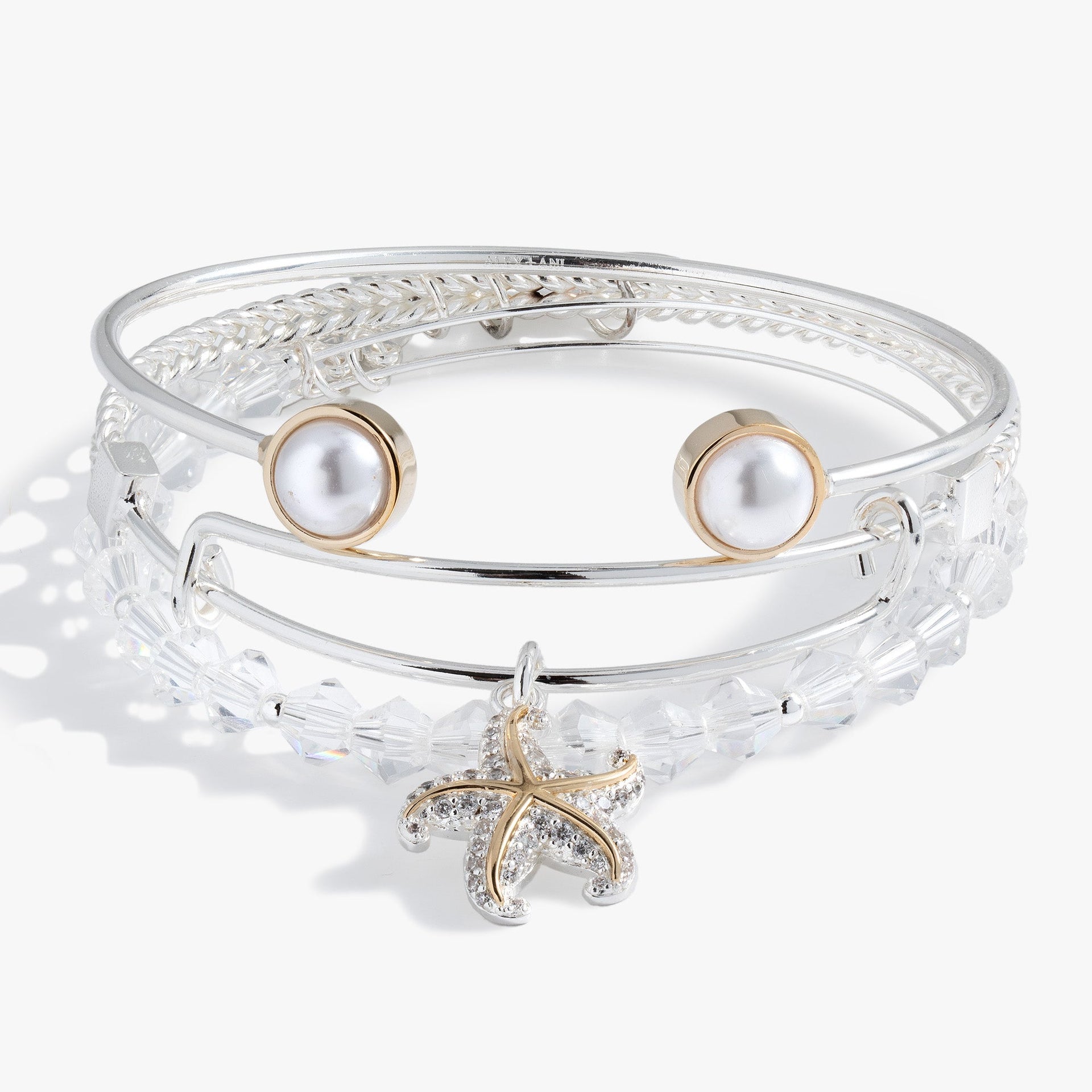 A set of three two-tone starfish, crystal, and pearl bangles worn as a stack.