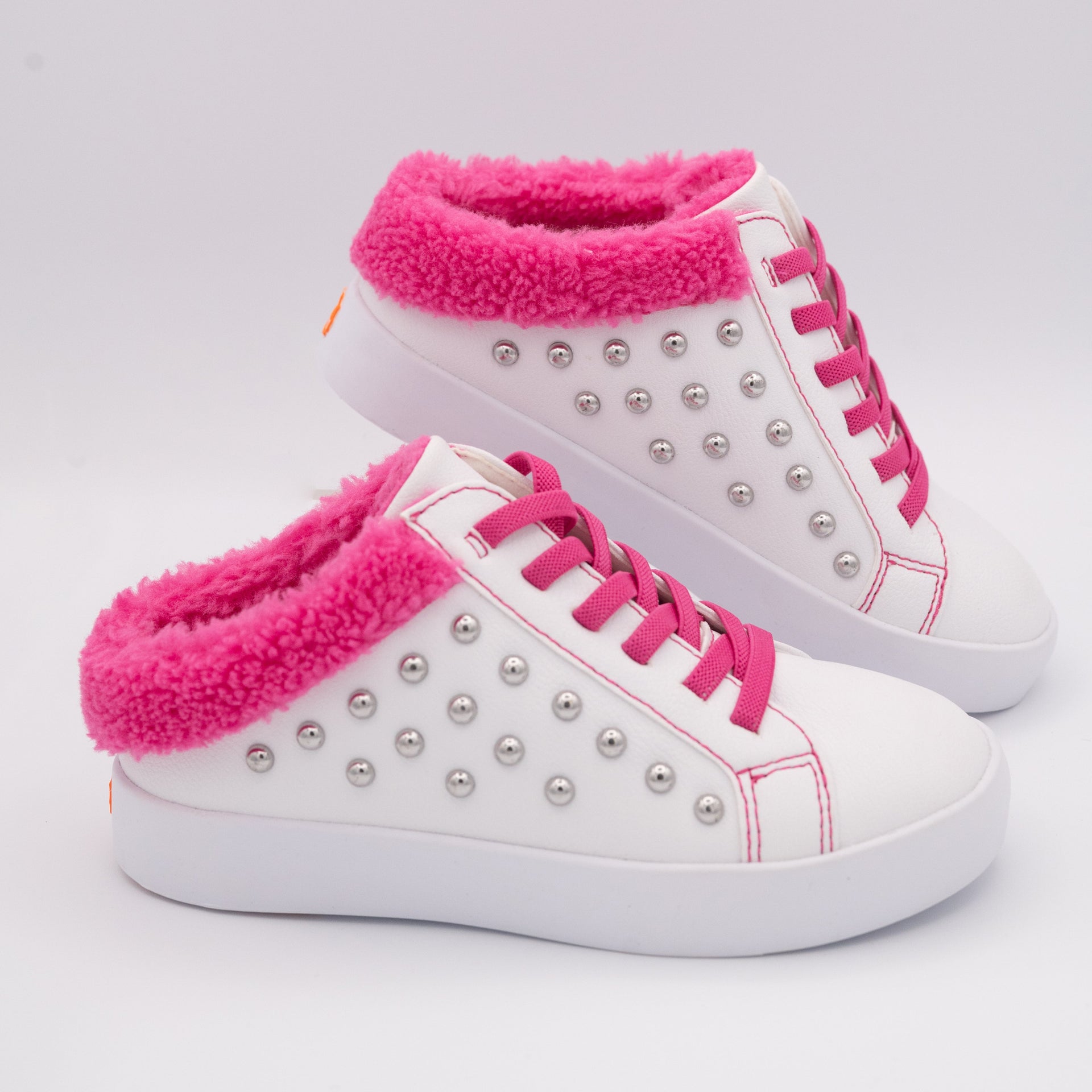 White slip-on fashion sneakers with silver studs and hot pink fleece trim on a white background