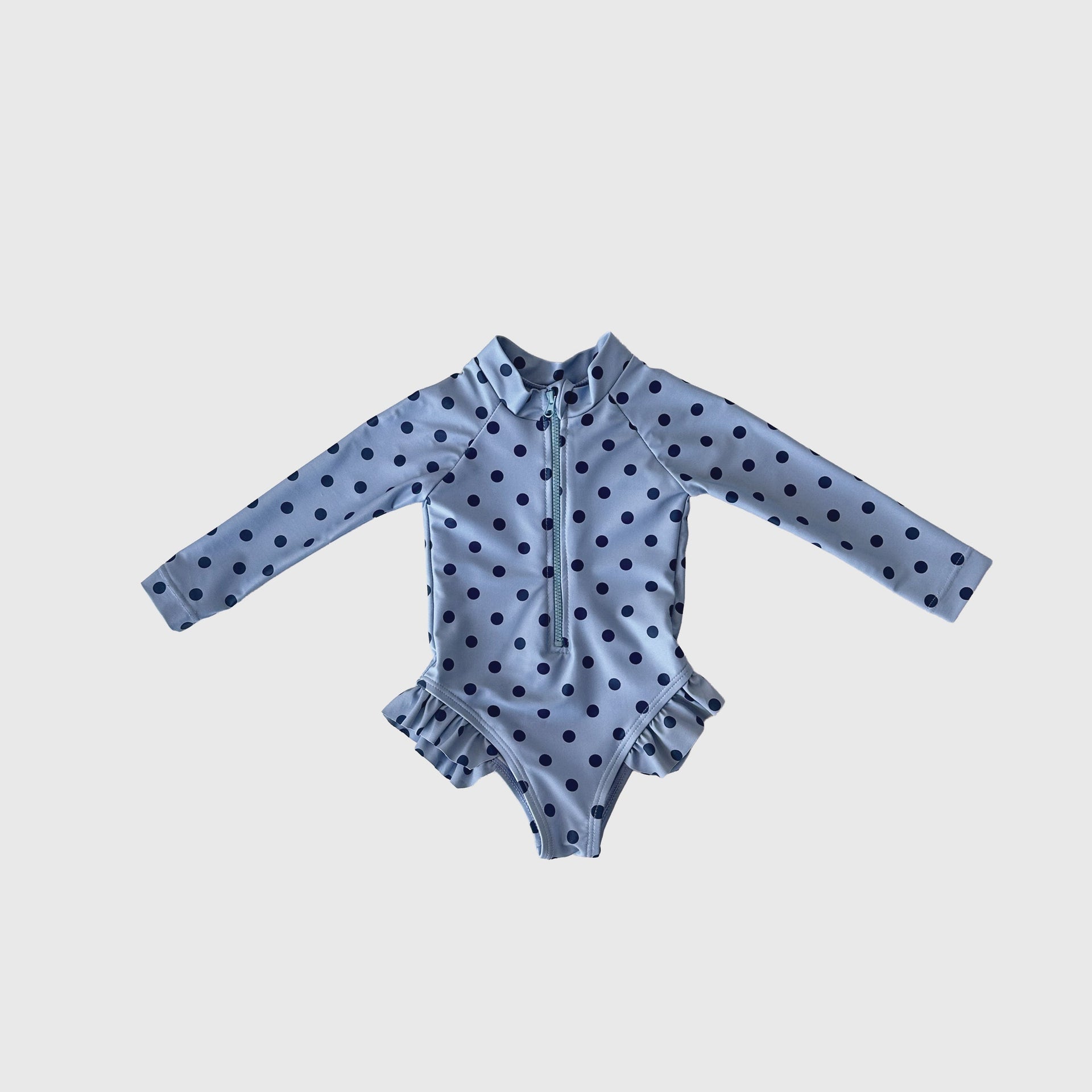 Girl wearing a long sleeve Sully polka dot one-piece swimsuit with ruffle leg details