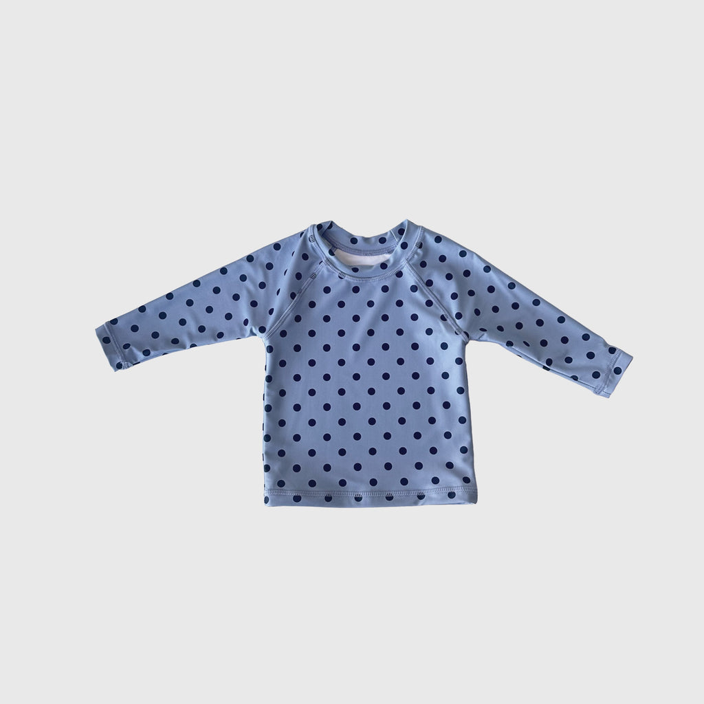 Child wearing a navy and light blue polka dot Sully rash guard on the beach