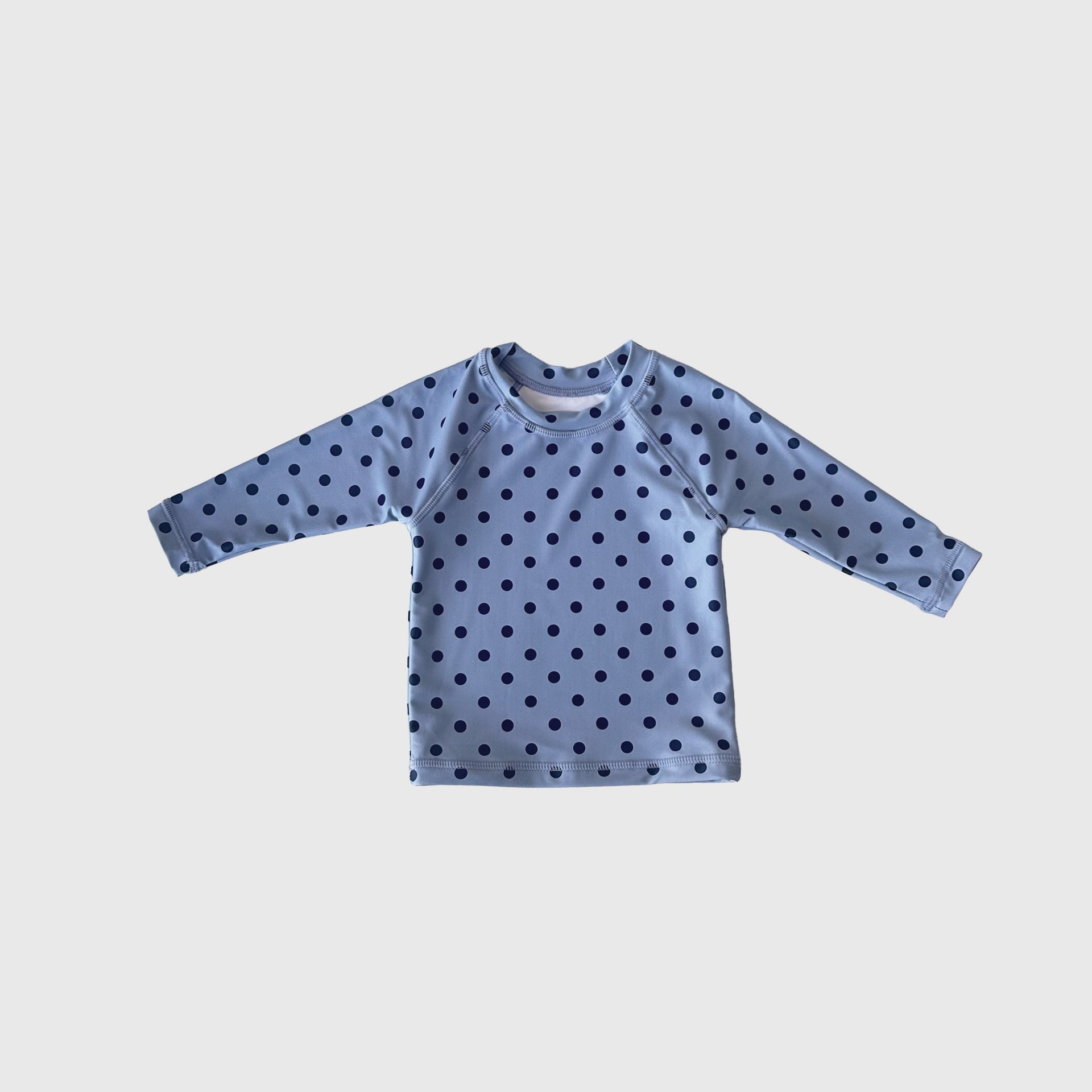 Child wearing a navy and light blue polka dot Sully rash guard on the beach