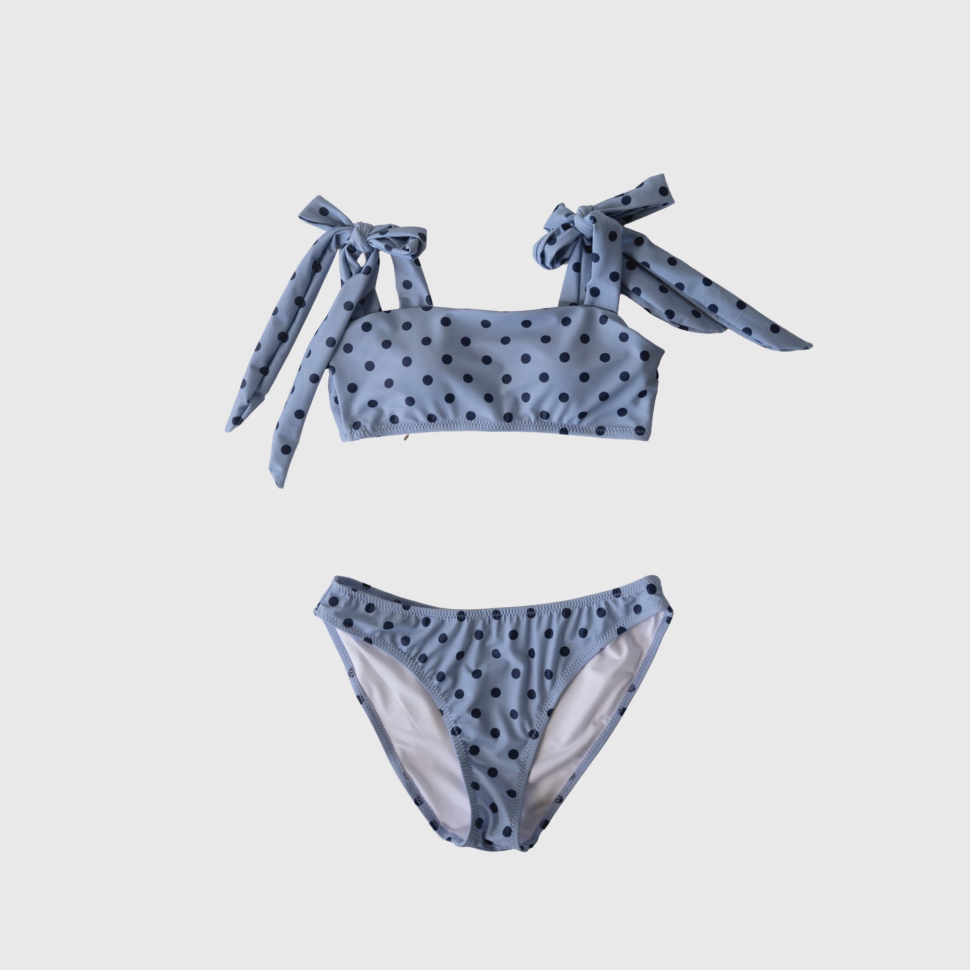 Woman wearing a classic polka dot bandeau two-piece swimsuit with adjustable shoulder ties in light-blue.