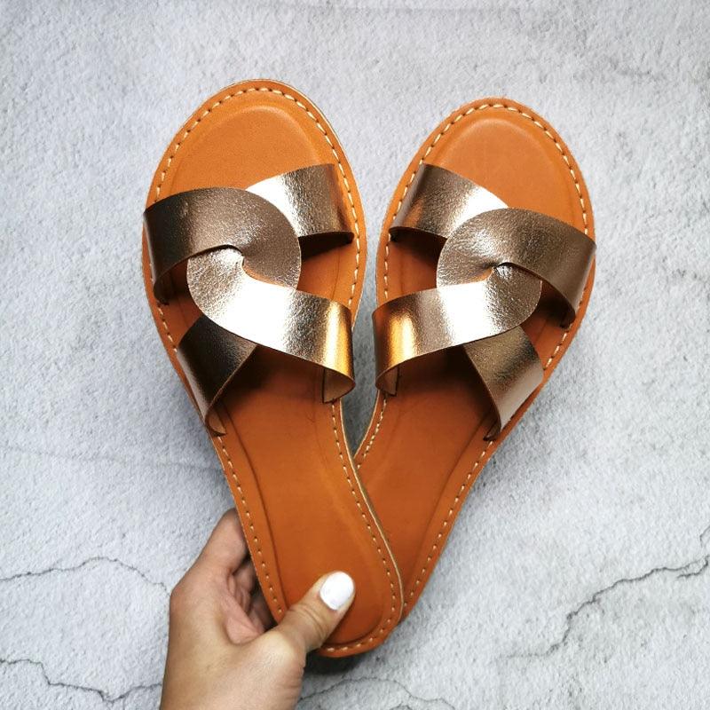 A pair of minimalist women's flat leather slides in tan featuring a cross-strap design.