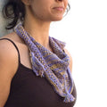 A woman wearing a handcrafted knit shawlette in soft lavender and sandy beige variegated yarn, styled over a summer dress.