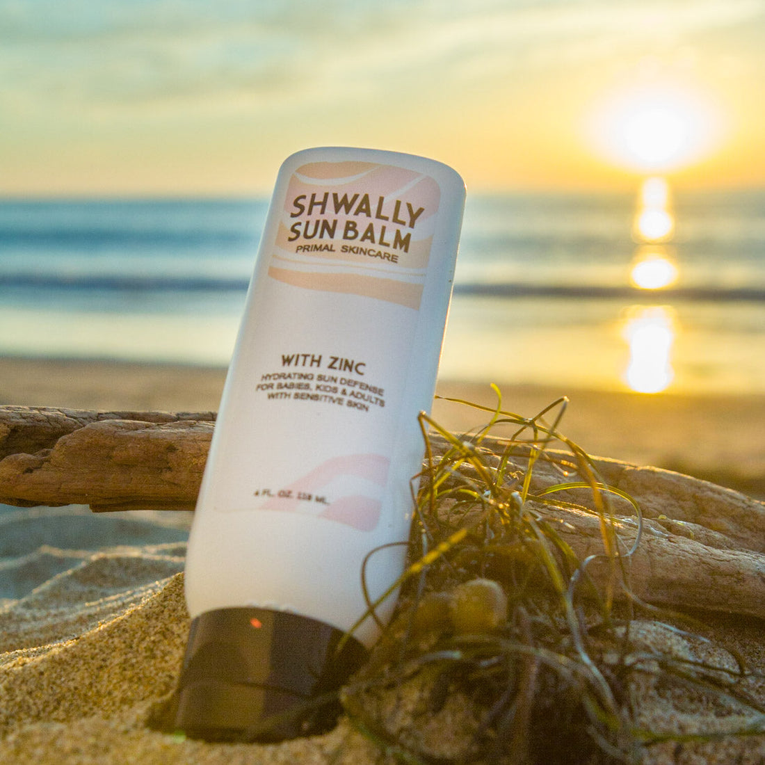 Shwally Sun Balm bottle on a beach with sunset in the background