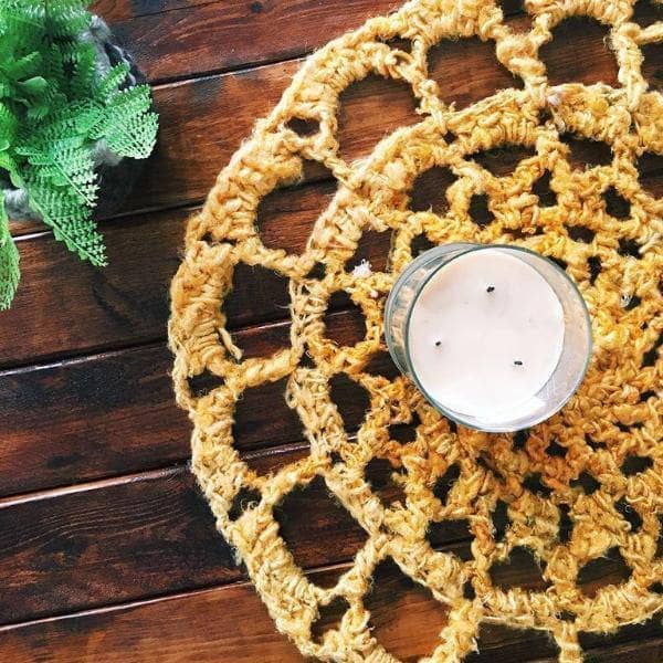 Close up of a vibrant yellow, pink, and blue crochet mat, a bohemian style home decor project made from banana fiber yarn.