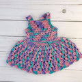 A handmade crochet sundress for an 18-inch doll in variegated pink, purple, and turquoise yarn with a scoop neck and button closure.
