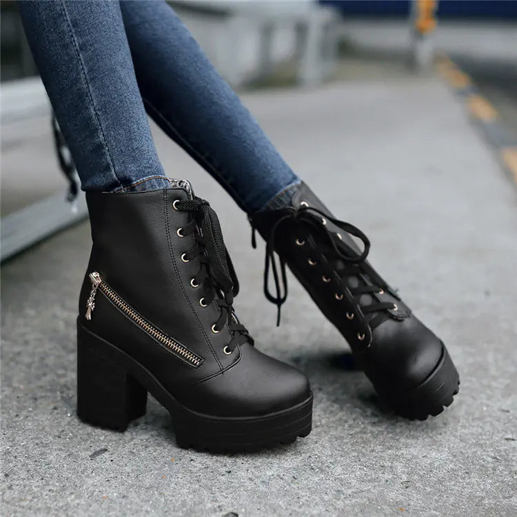 Side view of women's black platform ankle boots with chunky heels and side zipper detail on a concrete sidewalk.