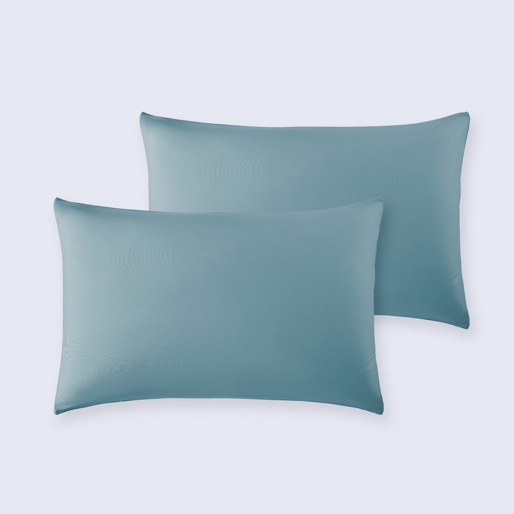 A set of two soft, blue cooling pillowcases on a white bed sheet.