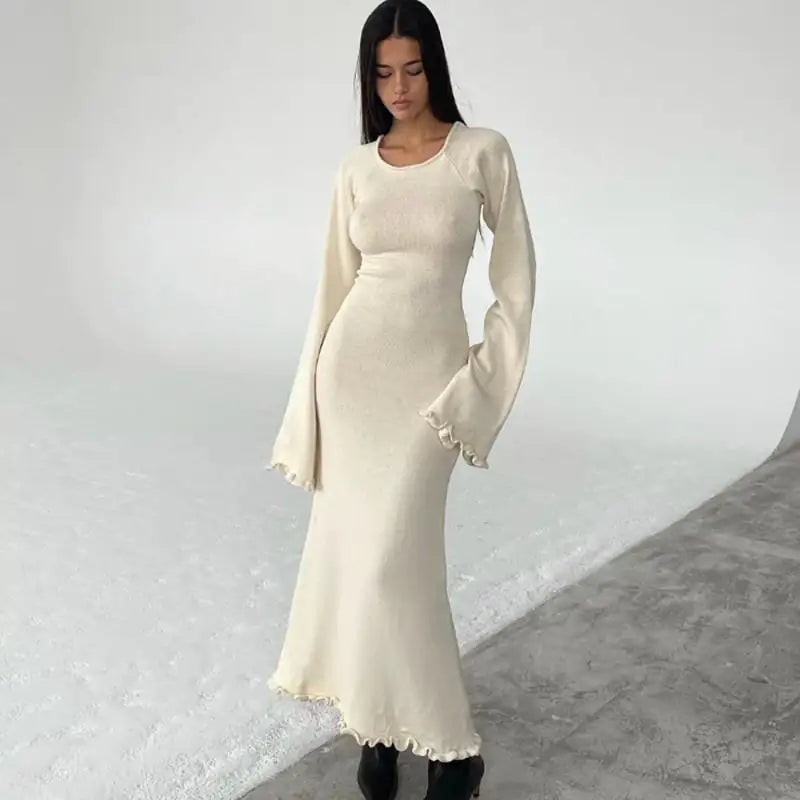 A woman wearing a cream-colored long-sleeve knitted maxi dress with a ruffle hem against a plain white background.