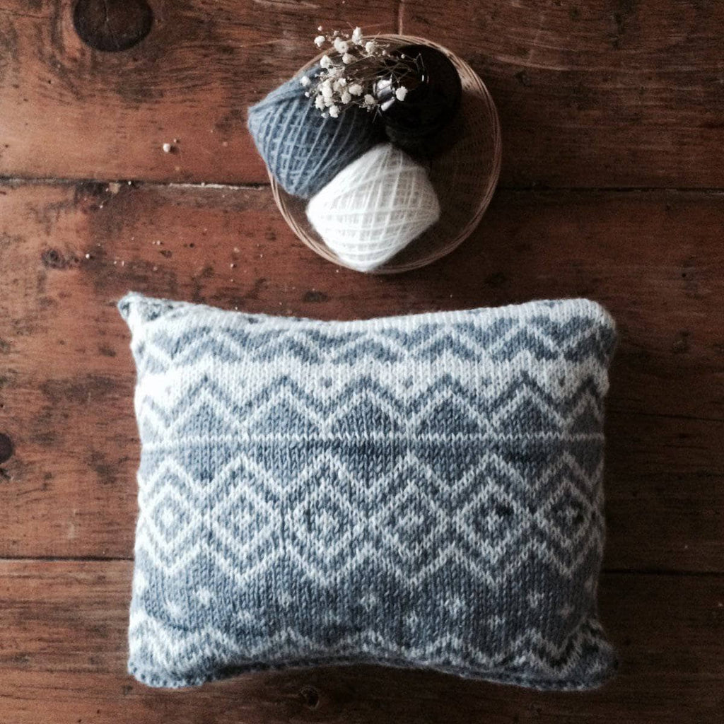 Geometric knit throw pillow in neutral white and grey colors, styled on a modern sofa
