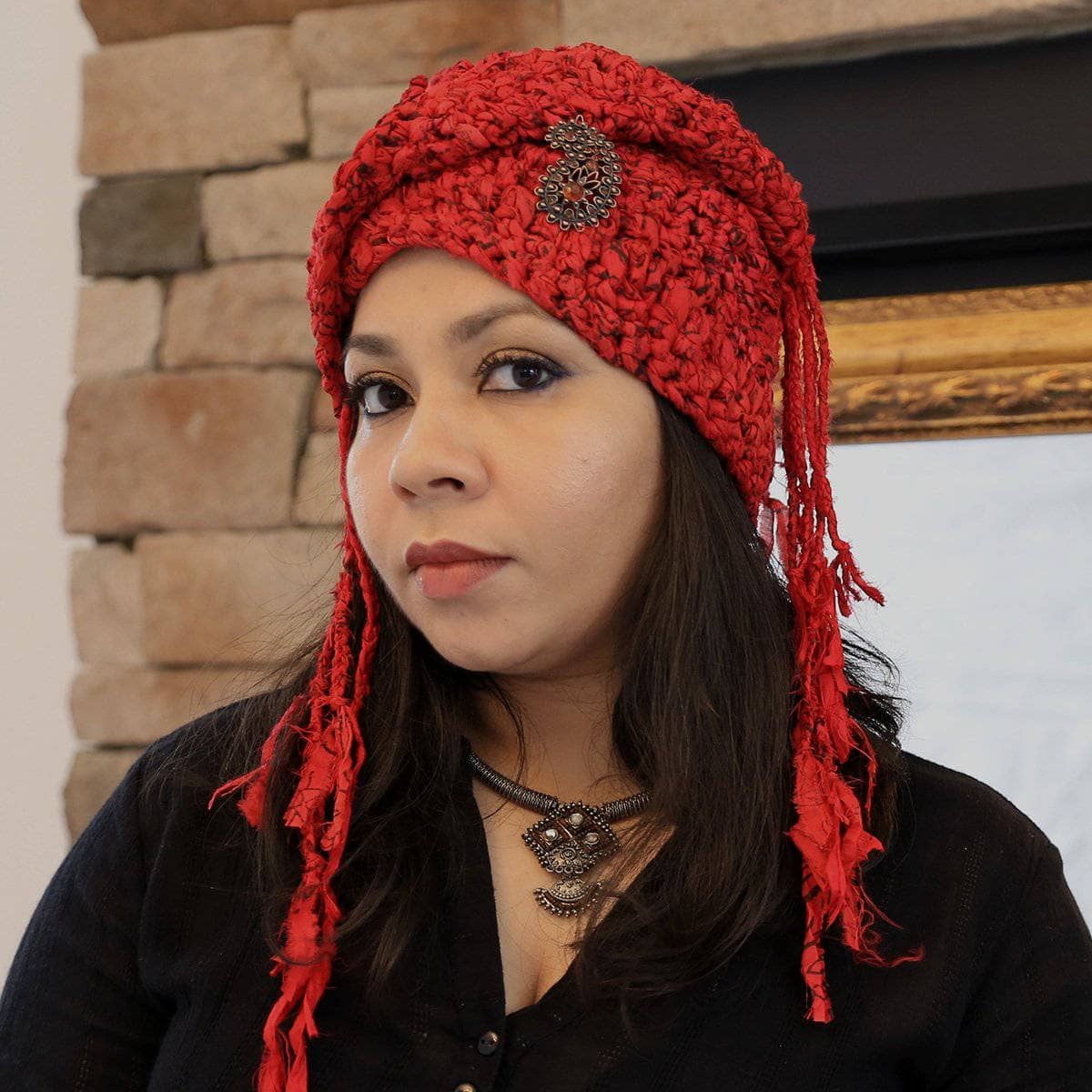 A close-up of a crocheted red headscarf with fringe, inspired by a traditional Taj crown design.
