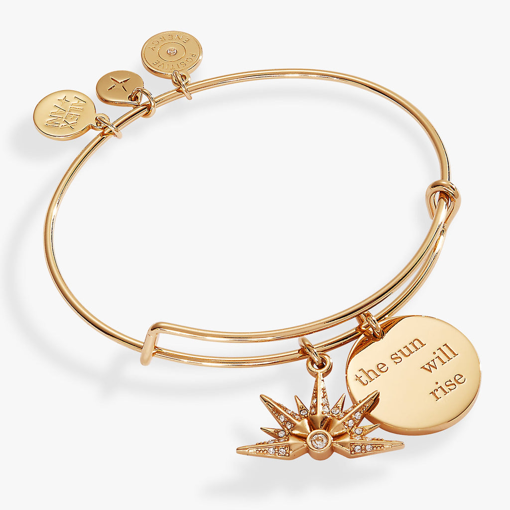 Gold-tone expandable bangle featuring a 'The Sun Will Rise' engraving and a crystal-accented sunrise charm