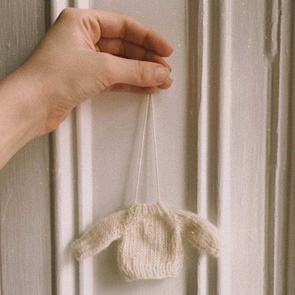 Miniature hand-knitted sweater ornament hanging on a pine tree branch