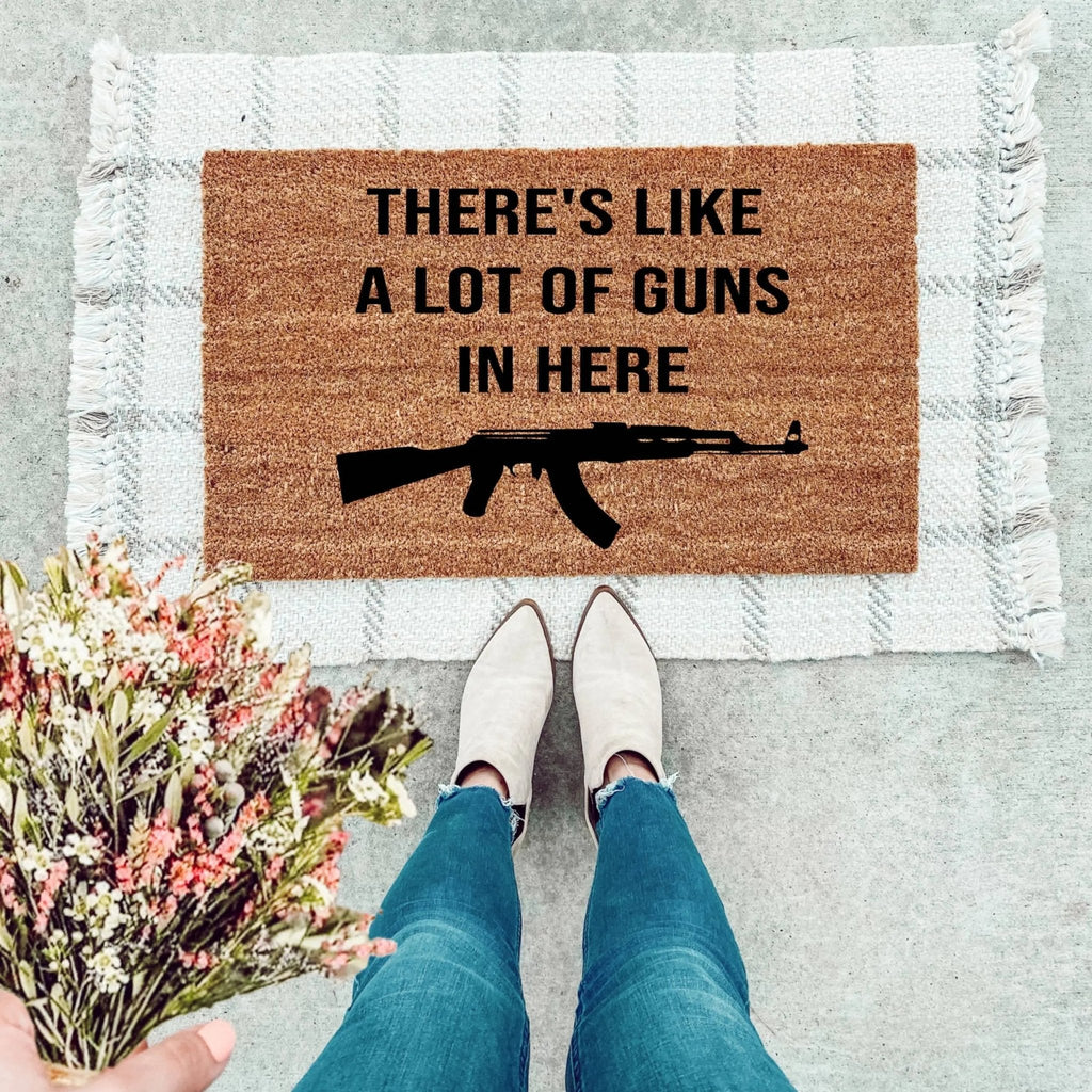 A rustic brown coir doormat featuring black lettering that says There’s Like A Lot Of Guns In Here.