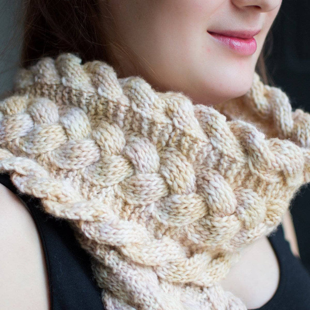 A soft, cream-colored reversible cabled knit scarf styled for a cozy winter look.