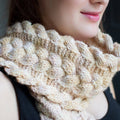 A soft, cream-colored reversible cabled knit scarf styled for a cozy winter look.