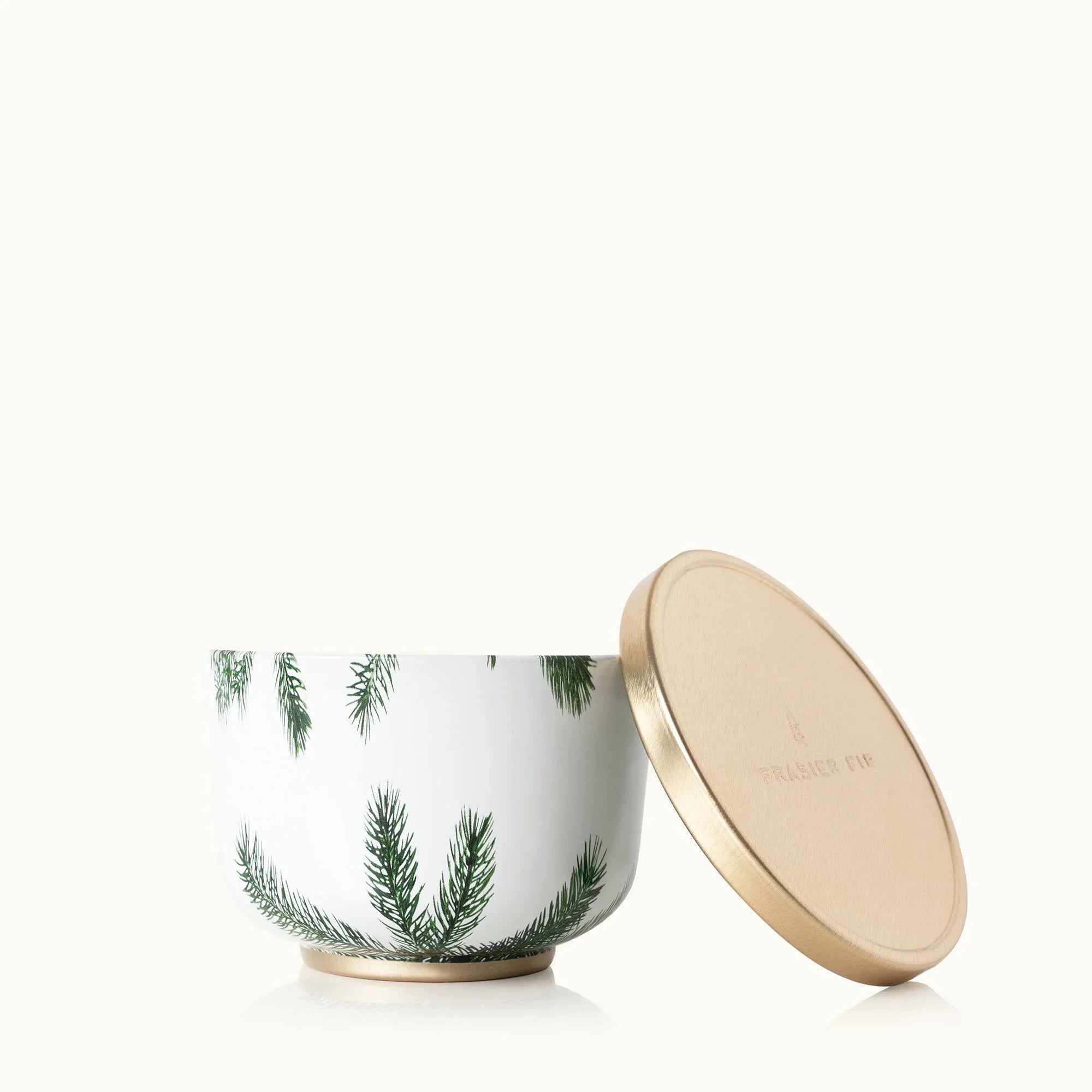 Frasier Fir candle in a metal tin with a gold lid on a festive holiday background.