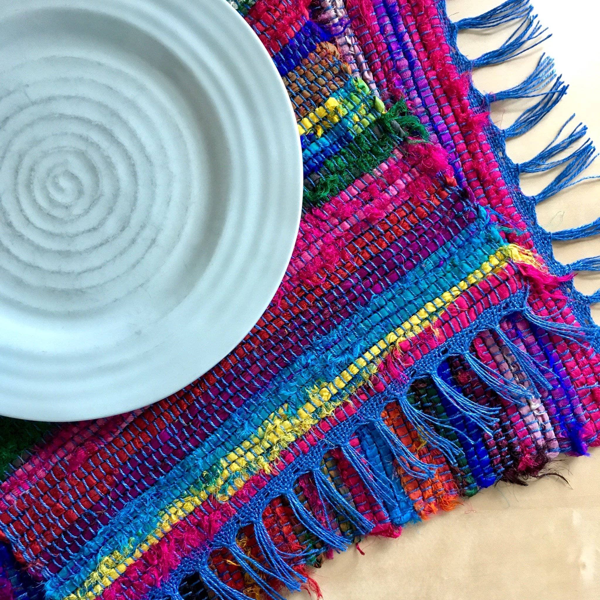 Colorful bohemian-style woven placemat with vibrant striped pattern in hot pink, electric blue, lime green, yellow, and orange.