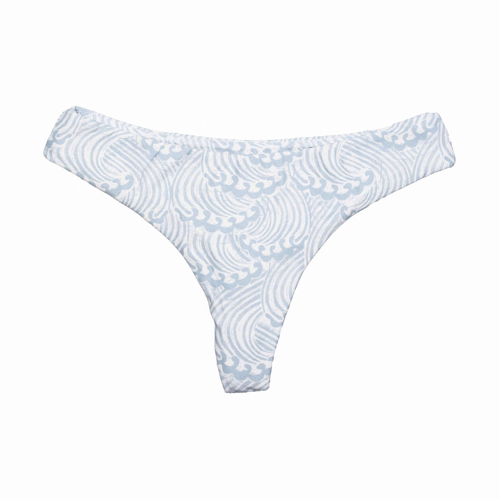Model wearing a white cheeky Whale Tale bikini bottom in a minimalist coastal setting.