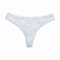 Model wearing a white cheeky Whale Tale bikini bottom in a minimalist coastal setting.