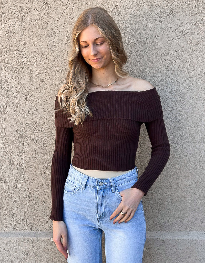 Model wearing a dark chocolate brown ribbed off-shoulder cropped sweater with a tie-back detail.