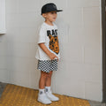 Child wearing an Easy Tiger graphic crew neck top and coordinating checkered shorts set outdoors.